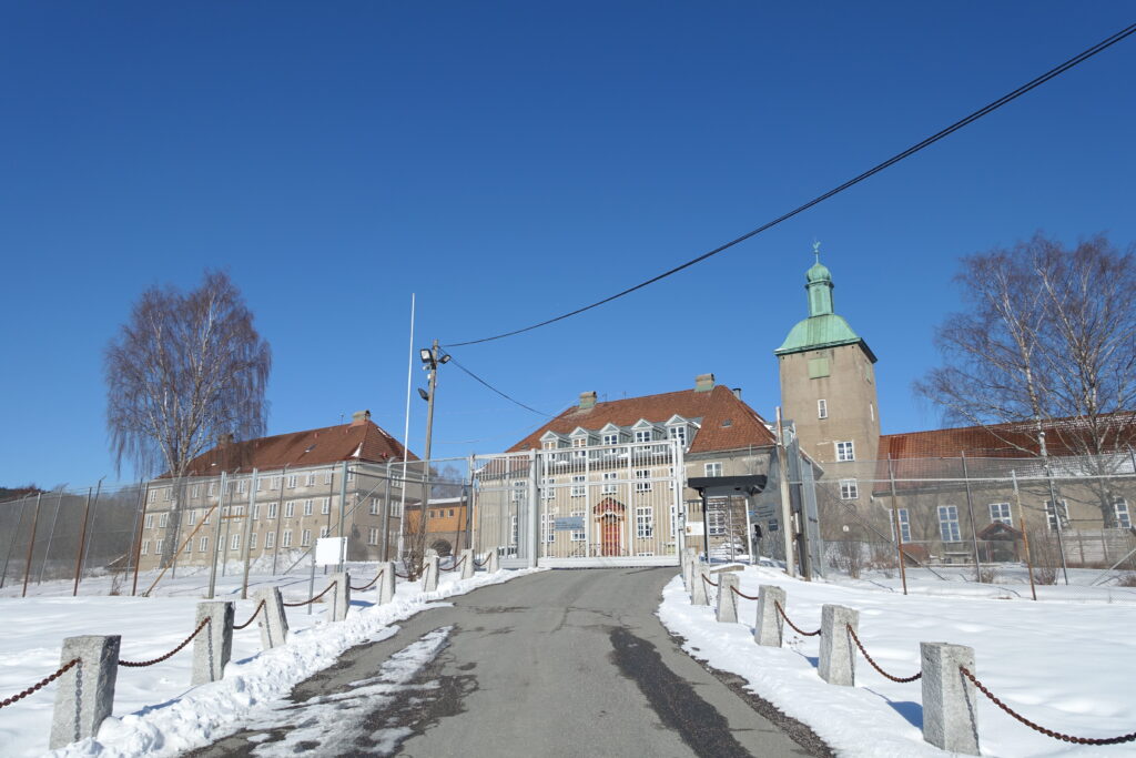 Grå fengselsbygninger i vinterlandskap med blå himmel