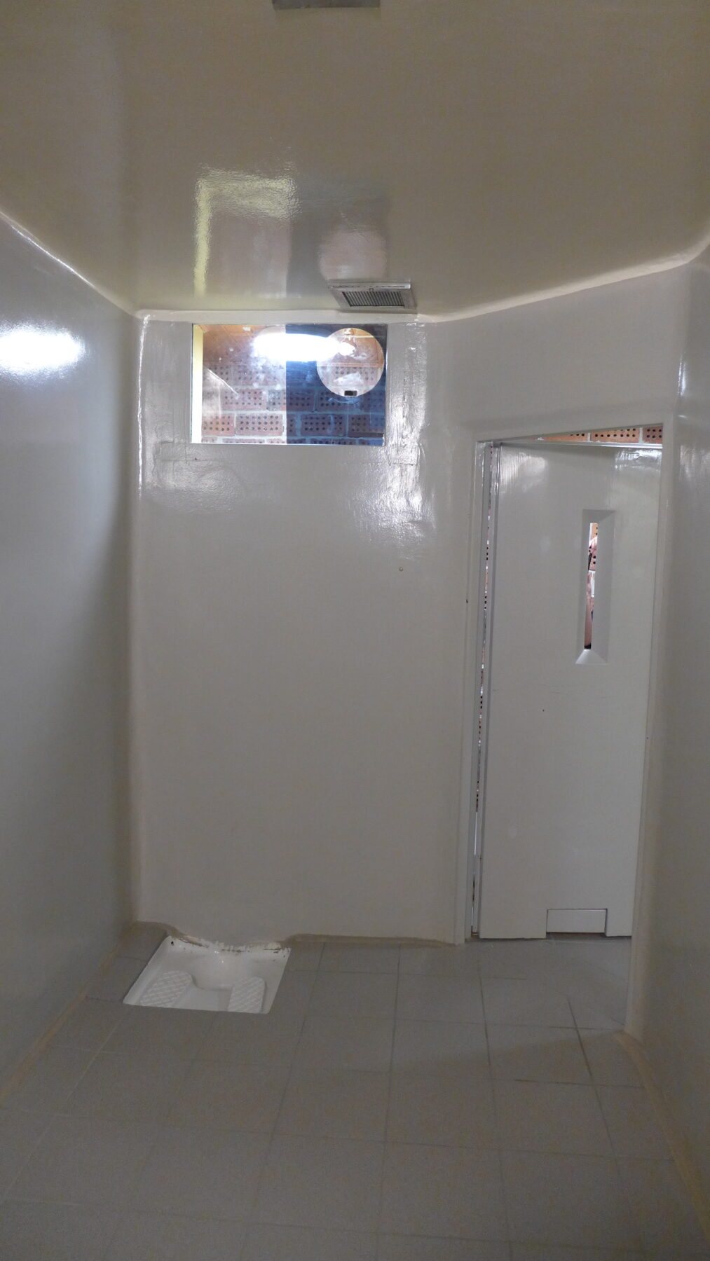 Sikkerhetscelle med hvite dør og hvite vegger.