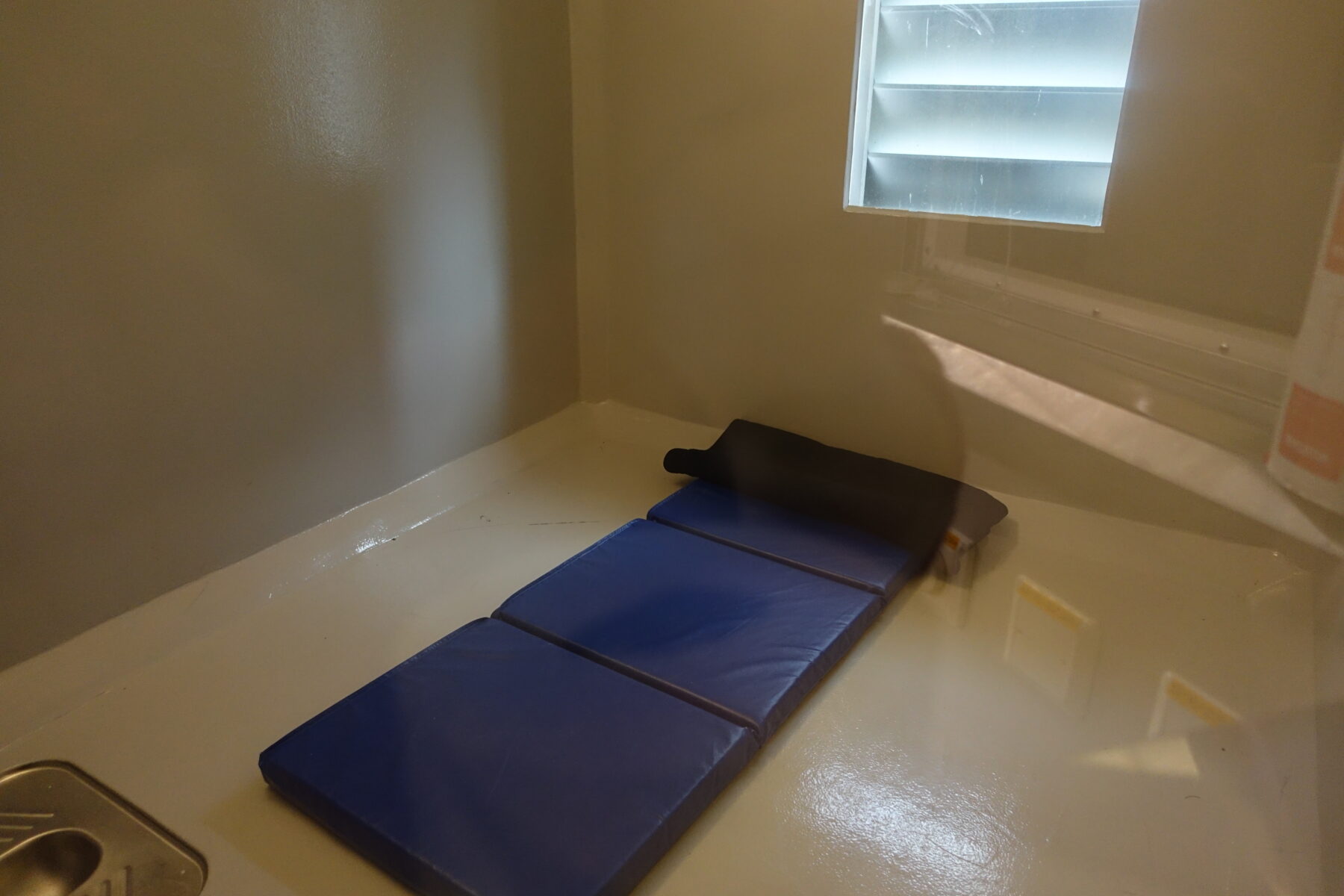 Blå madrass på golvet i fengselcelle